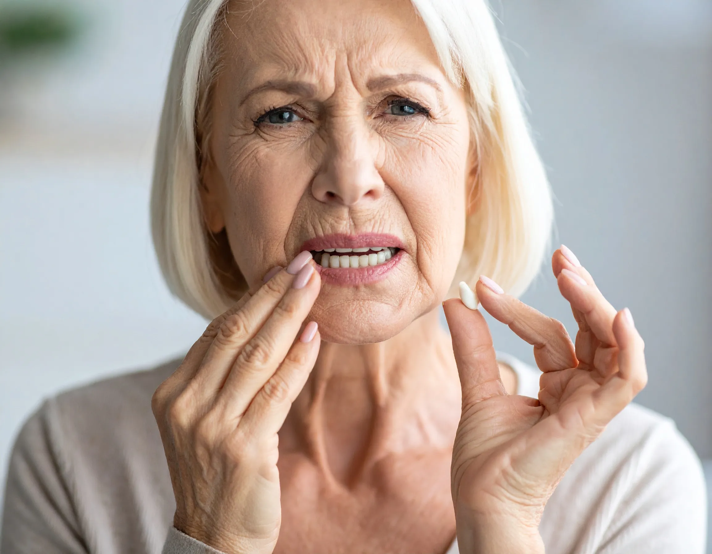 En kvinna som tappat en bit av en tand, som hon håller i, och ser orolig ut.