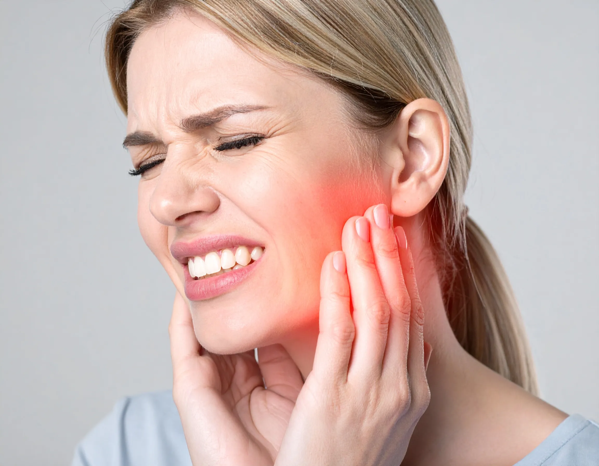 En person som håller sig för kinden på grund av tandvärk.